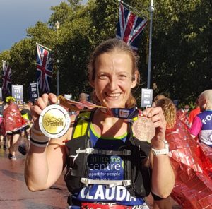 Claudia holding up two medals post London Marathon with a huge smile