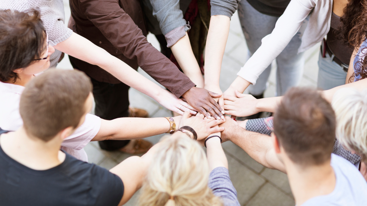 Group of people standing round in a circle holding their hands in the middle.
