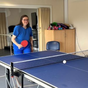 Smiling lady playing a game of table tennis. Her opponent (out of picture) has just hit the ball into the next.