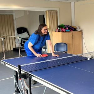 Smiling lady playing a game of table tennis. Her opponent (out of picture) has just hit the ball into the next.