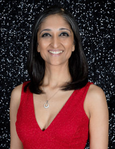 Headshot of a smiling young lady in a red dress with a glitter background.