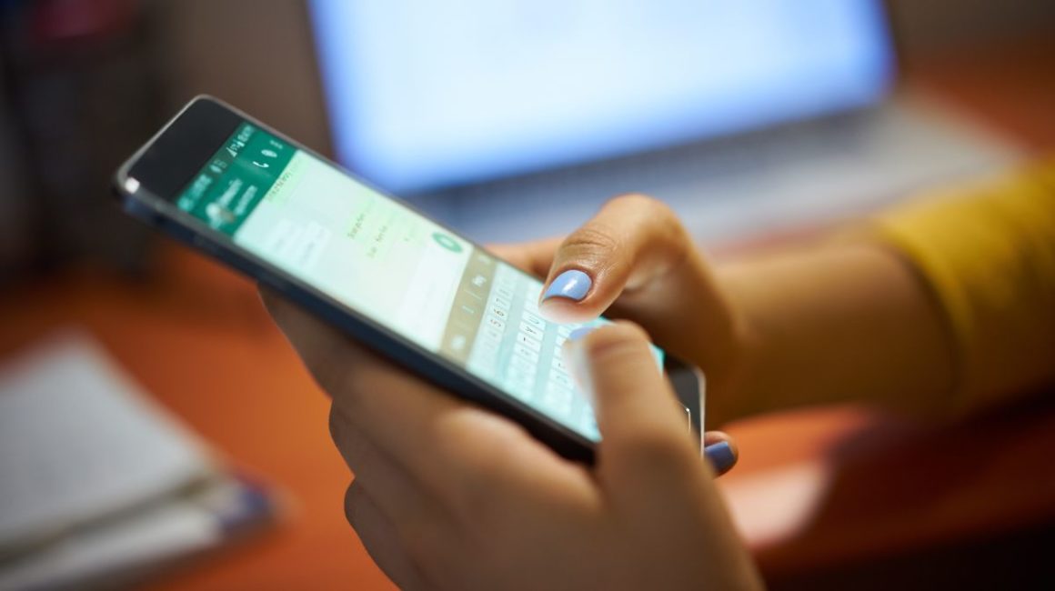 Image of someone looking at a smartphone screen which is displaying the WhatsApp app.