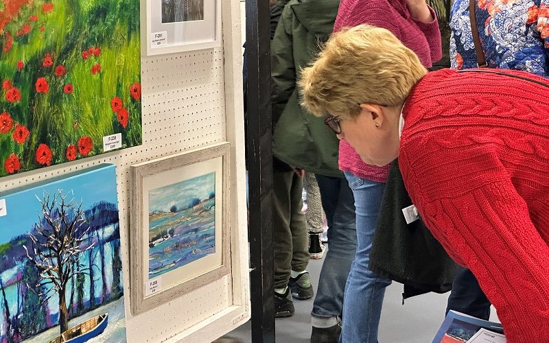 View of an art exhibition with a lady in a bright red jumper looking intently at a painting.