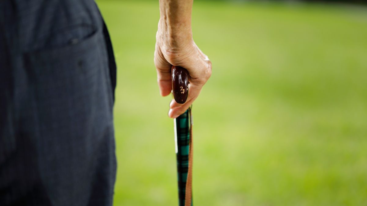 Close up of a man walking outside using a walking stick.