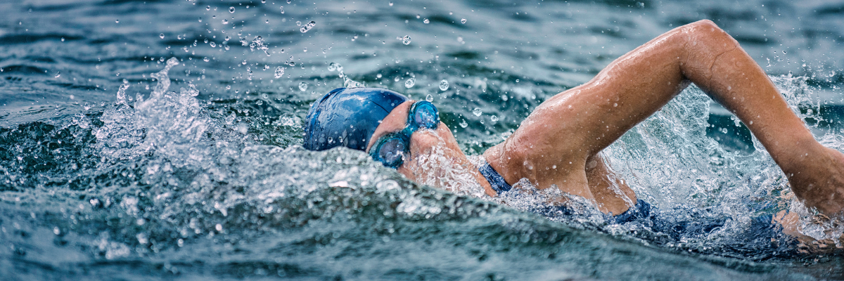 Person open water swimming. they ae wearing a dark blue swimming hat and blue goggles