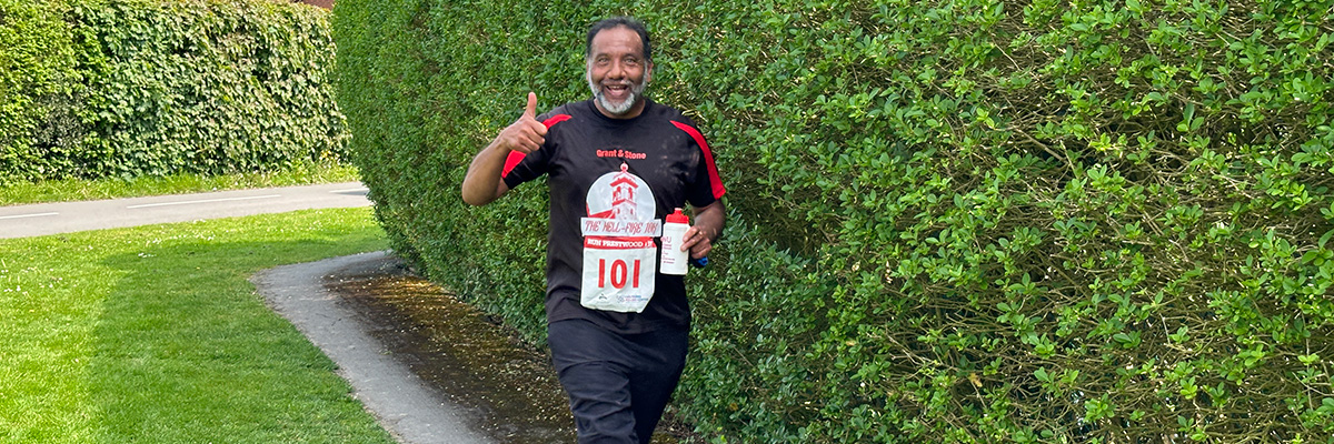 Smiling man taking part in a running race giving a big thumbs up.