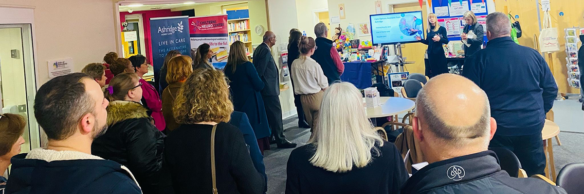 Group of people standing in a busy office atrium listening to someone at the front talk.